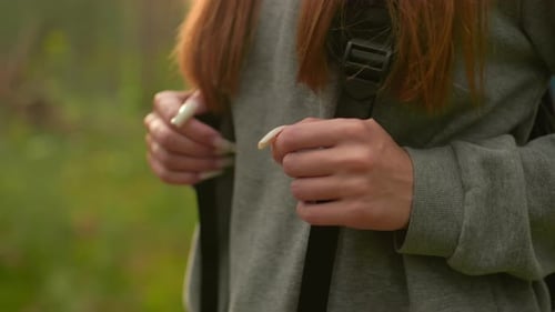Gros plan d'une femme aux ongles longs avec bretelles de sac à dos, randonnée dans une forêt luxuriante