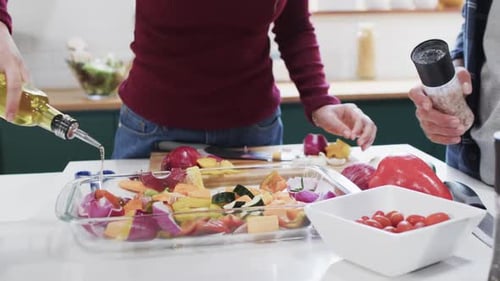 Sección media de una pareja diversa que prepara la cena en la cocina de su casa, en cámara lenta