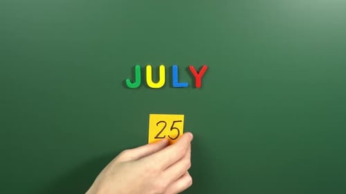 Hand sticking a sticker 25 July calendar day on school board. 25 date of July. Twenty fifth day