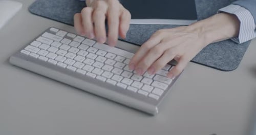 Nahaufnahme weiblicher Hände, die mit drahtloser Computertastatur tippen, während eine Geschäftsfrau am Schreibtisch arbeitet