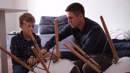 Father and Son Assemble Furniture From Small Parts Little Boy Helps His Father to Assemble a Chair