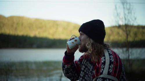 Norwegian Guy With Long Hair Drinking Coffee Near Mountain Lake. Closeup, Sideview