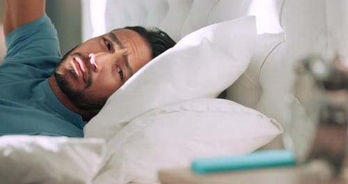 Man tired in bed with alarm time clock to wake up from sleeping in house or home bedroom on spring