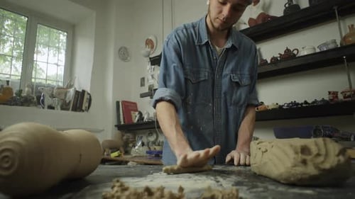 A Caucasian Male Ceramist Rolls Pliable Clay on a Table