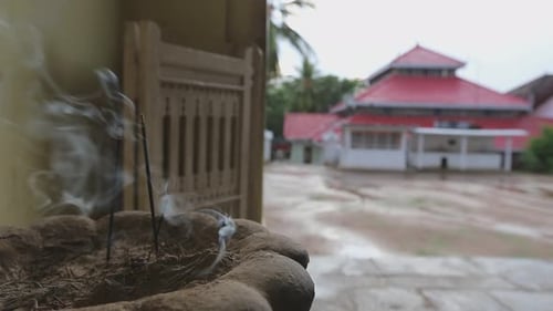 Close up view of incense sticks burning in front of a beautiful Asian Buddhist temple having red roo