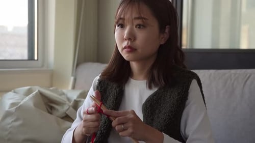 Young Woman Knitting with Red Yarn Indoors