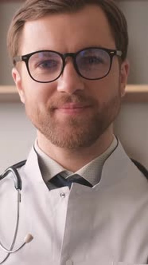 Portrait of a Handsome Young Doctor in a White Uniform and Glasses Standing on a Background