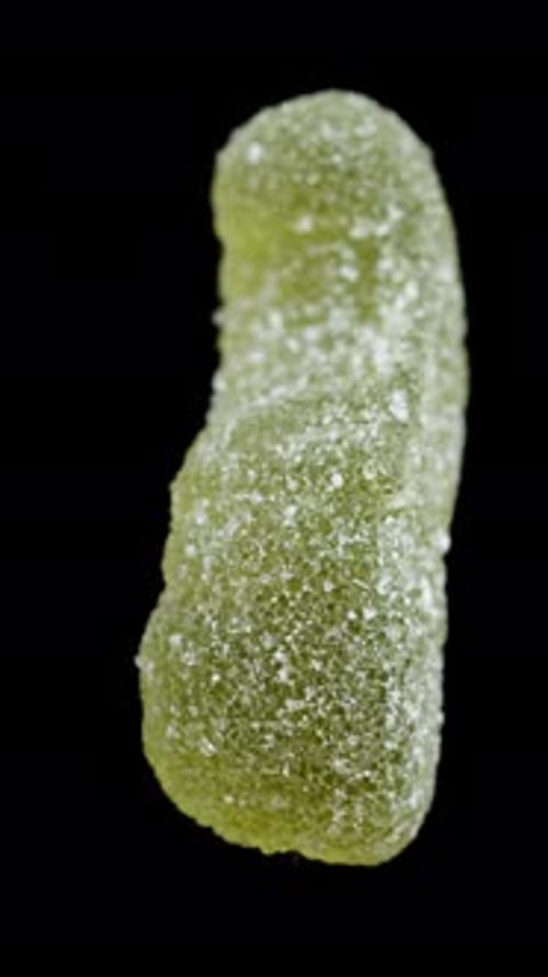 Vertical video. A gummy candy in the shape of a worm or larva, dusted with sugar. It rotates.