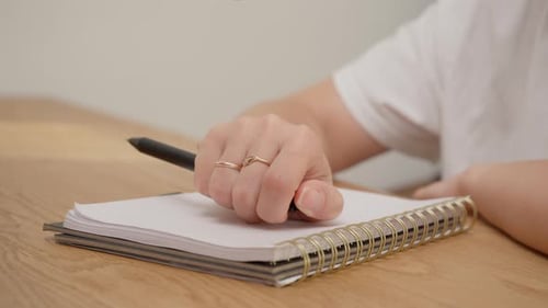 Female hand compulsively clicking black pen over spiral notebook with audio