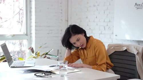 Young office worker is working late into the night at her desk in office, she grapples with stress