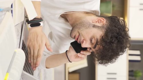 Young Adult Talking on Phone and Typing on Laptop