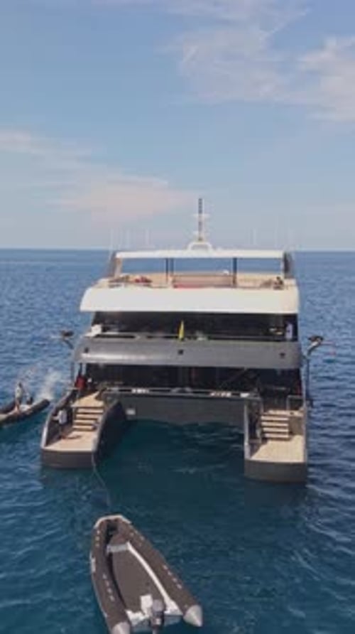 Vídeo aéreo vertical de un lujoso catamarán descansando cerca de un paisaje volcánico navegando en una pequeña lancha