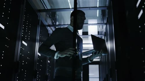 Male IT Engineer Opens Server Cabinet while Holding Laptop. He Works in Big Data Center
