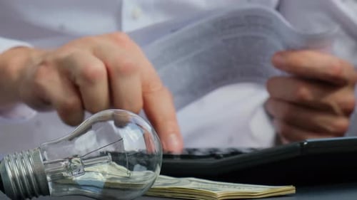 Electric Light Bulb Man Hands Counting Expenses Bills on Electricity Banknotes of Dollar Cash