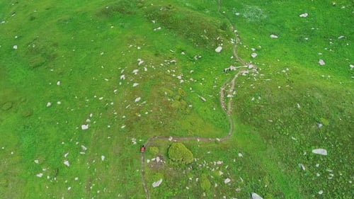 Blick von oben auf einen wandelnden Mann, der dem Pfad zwischen grünen Wiesen in den kasachischen Bergen folgt