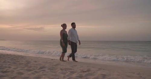 Romantic couple walking hand in hand on a tropical beach at sunset