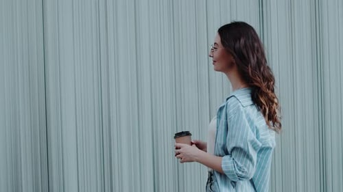 Side View Portrait of Young Beautiful Asian Woman Wearing Glasses Smiles and Holds Coffee Cup at the