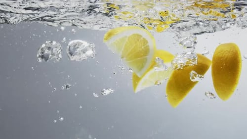 Underwater shot of lemon quarters falling in fresh clear water with big bubbles. Close up, slow moti