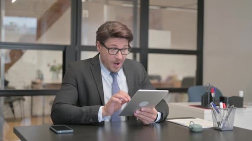 Middle Aged Businessman Celebrating Success on Tablet in Office