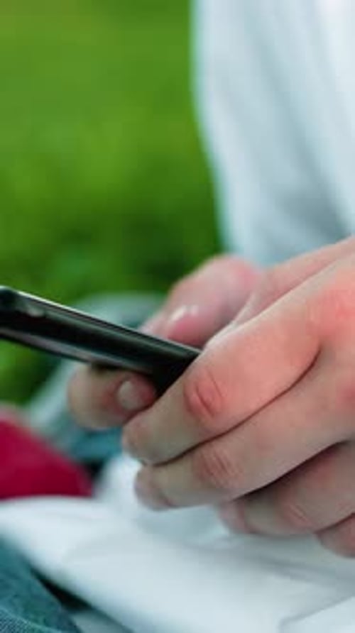 Closeup Hand Using Smartphone in Grass Field with Red Cloth Nearby