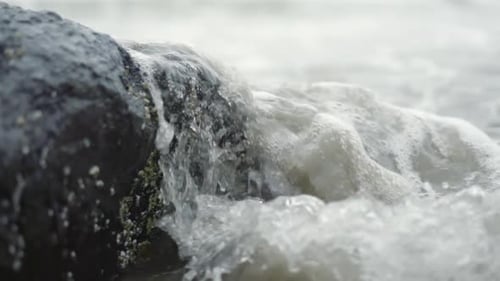 Ocean waves crashing over barnacle covered rock on beach in slow motion