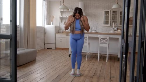 Mujer afroamericana emocionada en una báscula comprobando el éxito de la pérdida de peso