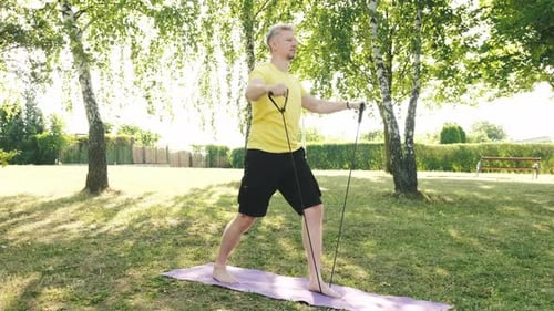 Athletic Young Man Doing an Exercises for the Shoulders on a Grass Outdoors