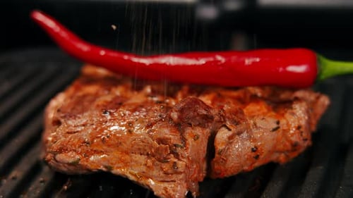 Closeup Spices Falling on Grilled Tasty Meat and Red Hot Pepper on Grill Closeup Delicious Food