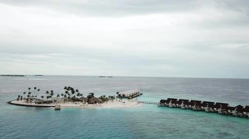 O drone sobrevoa uma ilha com vilas aquáticas em um resort nas Maldivas. Água azul e turquesa. 4K
