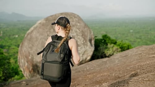 Woman with Backpack Hikes Up Rocky Mountain Peak Explorer Reaches Summit Enjoys Green Landscape