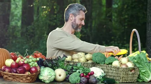 Man shucking corn surrounded by fresh vegetables outdoors