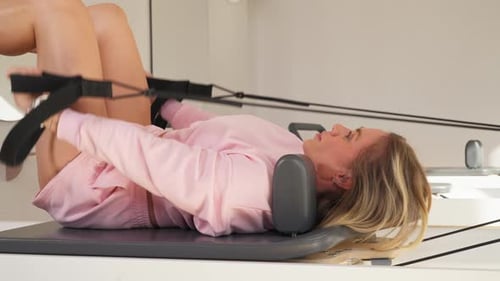 Woman Practices Pilates on a Reformer Machine