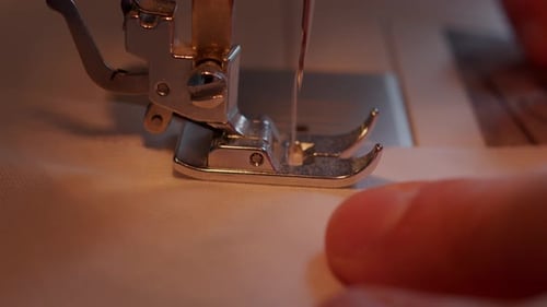 Close side view of needle moving through sewing machine foot into fabric moved through by the operat