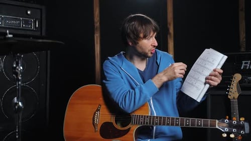 Man Teaching Guitar Using Music Sheet in Studio