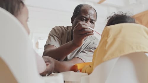 Man Feeding Two Infants in High Chairs