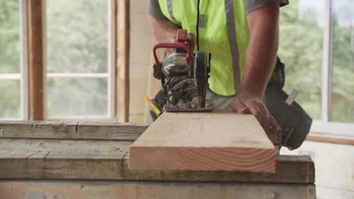 Carpenter Cutting Wood Plank with Power Saw Indoors
