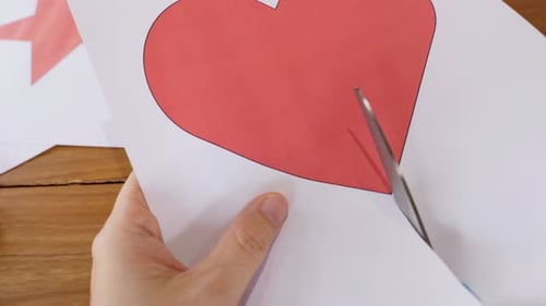 Close-up of hands cutting heart shape on paper using scissors