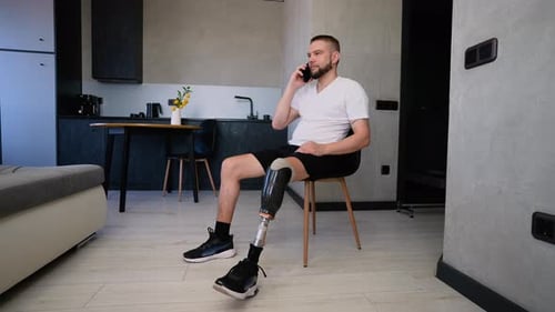 A Man with a Prosthetic Leg Sits Comfortably in His Stylish Apartment Smiling While Talking on the