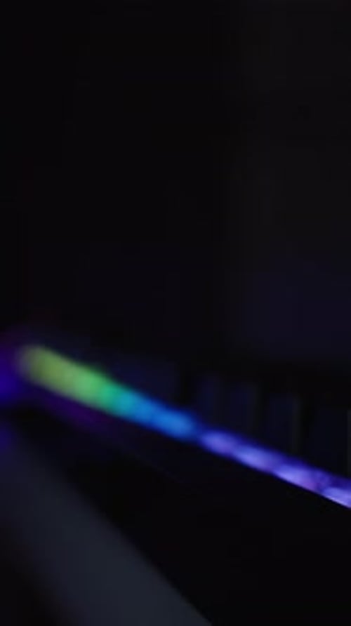 Vídeo vertical. Teclado negro con retroiluminación de arcoíris en la oscuridad y PC para juegos