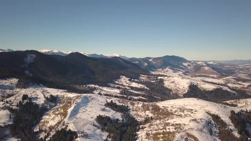 Luftaufnahme eines kleinen Dorfes mit verstreuten Häusern auf schneebedeckten Hügeln im Winter und in nackter Dunkelheit