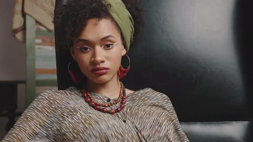 Junge ernsthafte Afroamerikanerin mit kreativem Make-up und traditionellen Accessoires aus Leder