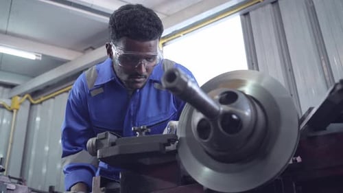 African mechanic worker using metal lathe machine at factory