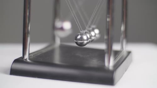 Slow motion: Newton's cradles swinging on a white minimal surface with a dark background in Slow Mot