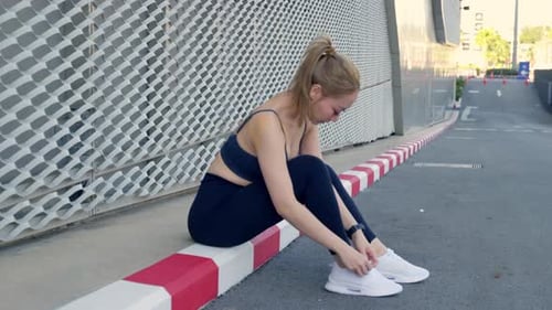 Young Woman Athlete Exercising Sport Lifestyle in City Sitting Roadside Curb Adjusting White Shoe