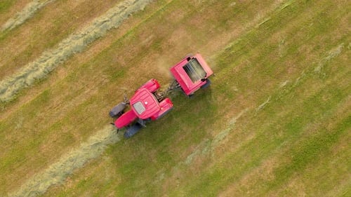 Tractor with Trailer Round Baler Collects Hay From Meadow for Forage Harvesting Aerial View