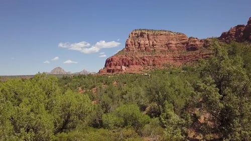 Drohne fliegt durch Baumwipfel im grünen Tal in Richtung der roten Klippe Sedona, Arizona