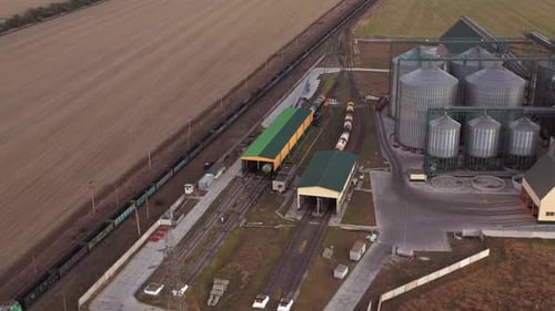 Langer Güterzug, der an einem Industriegebiet mit Lagerhallen vorbeifährt