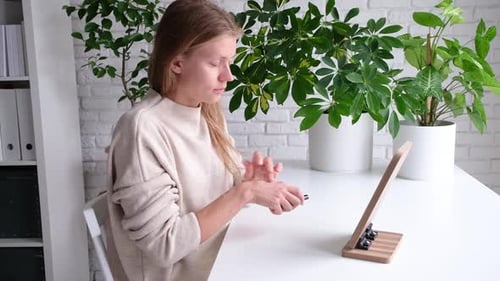 Woman Applying Makeup at Table with Houseplants