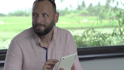 Man Uses Tablet and Drinks Coffee Indoors