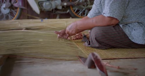 An Asian female farmer who is an elderly native basketry artisan weave mat from bamboo